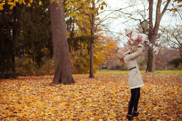 Junge Mutter und kleine Tochter gehen im Herbst spazieren. Mutter und Tochter spielen. Warmer Winter. Heller Herbst. Gemütlich.