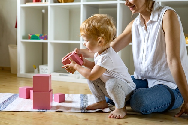 Junge mutter und kleines baby, die rosa würfel maria montessori ökologische materialien zusammenbauen