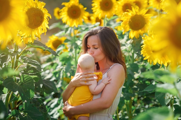 Junge Mutter und kleines Mädchen glücklich zusammen, umarmt in der Natur in einem Feld mit gelben Sonnenblumen.