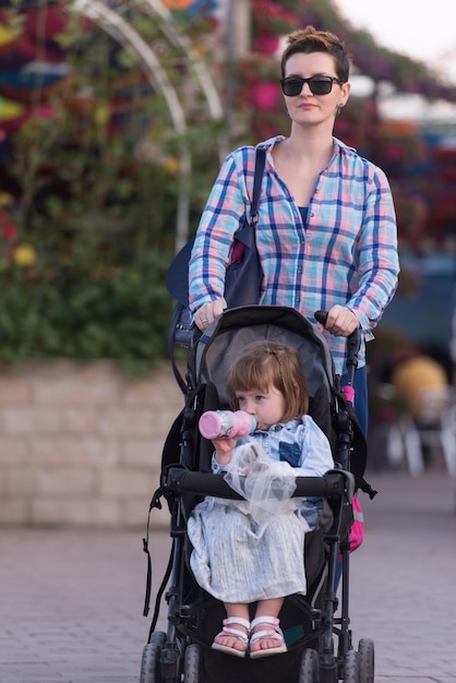 junge mutter und süßes kleines mädchen in einem kinderwagen genießen einen schönen tag im blumengarten