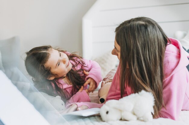 Junge Mutter und süßes Mädchen in rosafarbener Familie sehen Hoodie auf dem Bett im Kinderzimmer aus