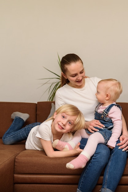 Junge Mutter und zwei Kinder, die auf Couch sitzen. Glückliches Familienkonzept. Vertikaler Rahmen.