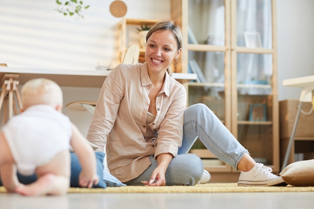 junge Mutter verbringt Zeit zu Hause und entspannt sich auf dem Boden mit ihrem niedlichen kleinen Sohn, horizontaler Schuss