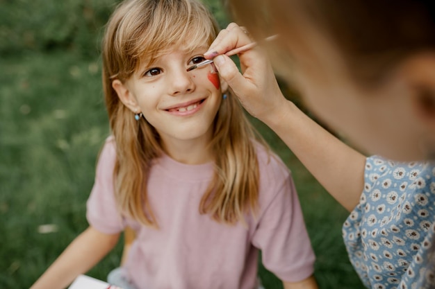 Junge Mutter zeichnet mit Farben auf ihrem Kindergesicht im Garten. Familienzeit.