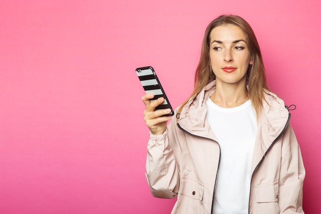 Junge nachdenkliche Frau, die Telefon hält, rosa lokalisiert.