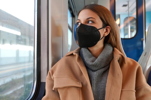 Junge nachdenkliche Frau in einer medizinischen Maske FFP2 KN95 im Zug, die durch das Fenster schaut. Konzept des Reisens und der Nutzung öffentlicher Verkehrsmittel während einer Pandemie.