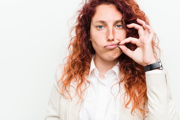 Junge natürliche rothaarige Geschäftsfrau mit den Fingern auf den Lippen, die ein Geheimnis halten