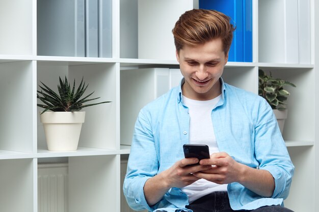 Junge navigieren in seinem Smartphone, während er lächelt und in einem Büro sitzt