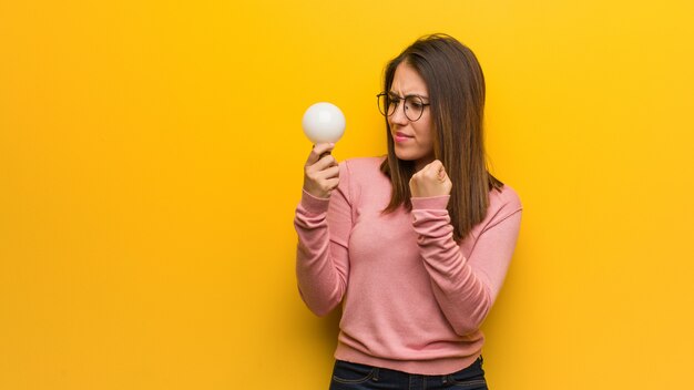 Junge nette Frau, die eine Glühlampe zeigt Faust zum vorderen, verärgerten Ausdruck anhält