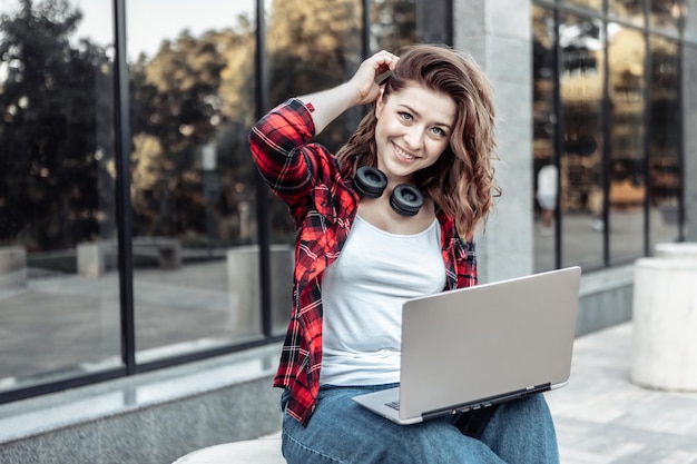 Junge nette Studentin, die draußen Laptop verwendet. Fernarbeit oder Bildungskonzept