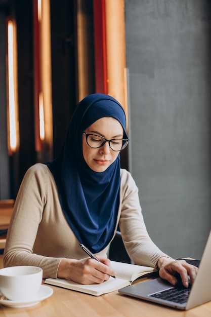 Junge nuslimische Frau, die online am Computer in einem Café arbeitet?