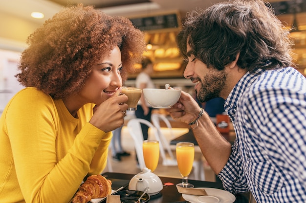 Junge Paare, die am Café frühstücken und einen Tee und einen Kaffee trinken, die einander betrachten