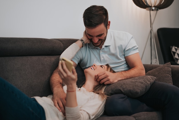 Junge Paare, die auf Sofa in ihrem Wohnzimmer sich entspannen.