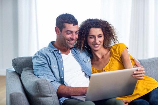 Junge Paare, die auf Sofa sitzen und Laptop verwenden