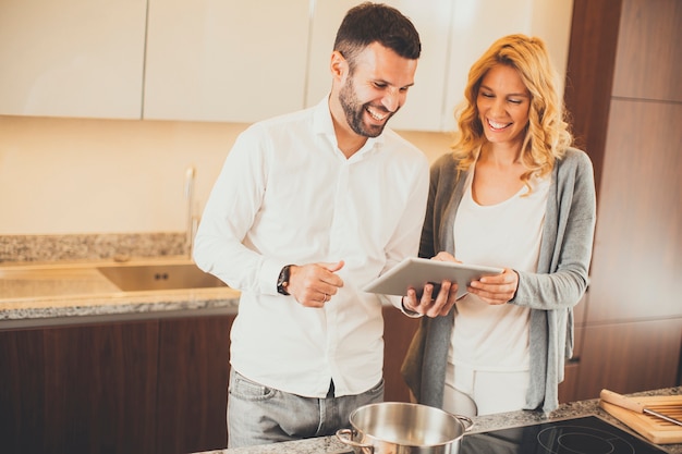 Junge Paare, die in der modernen Küche kochen und Tablette verwenden