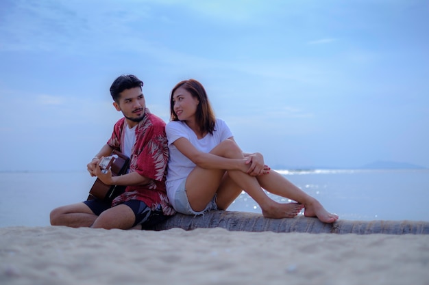 Junge Paare, die Musik spielen und zusammen am Strand singen