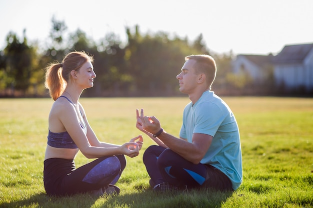 Junge Paare, die Spaß draußen haben. Mann und Frau, die zusammen draußen auf Feld mit grünem Gras bei Sonnenaufgang meditieren.