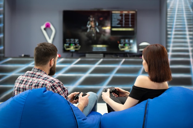 Junge Paare, die Videospiele spielen, sitzen auf Stühlen in einem Spielclub mit Controllern in ihren Händen