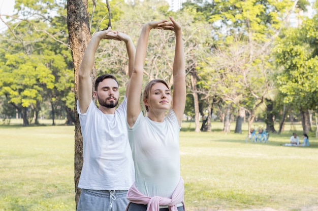 Junge Paare, die Yoga im Park spielen. Paare trainieren im Park.