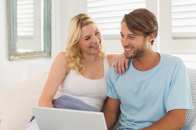 Junge Paare, die zusammen auf der Couch unter Verwendung des Laptops sitzen