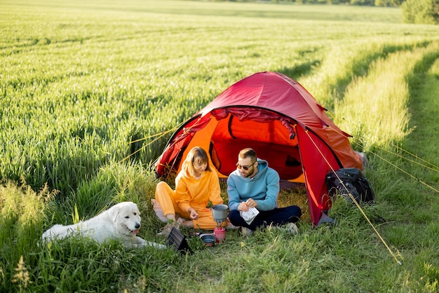 Junge Paare haben ein Picknick mit einem Hund in der Nähe des Zeltes auf der grünen Wiese
