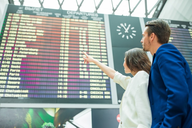 Junge Paare im internationalen Flughafen, der das Fluginformationsbrett betrachtet