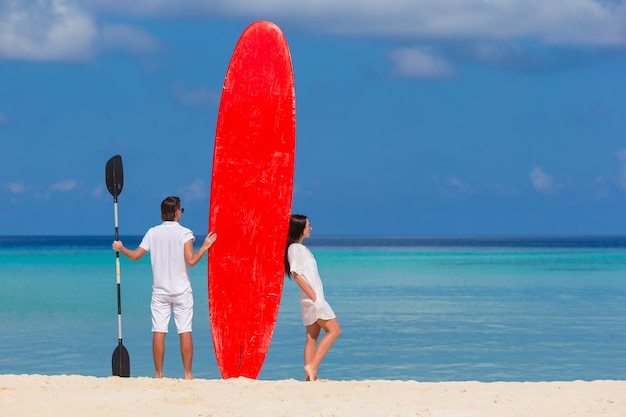 Junge Paare mit rotem Surfbrett während der tropischen Ferien