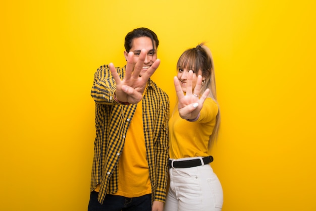 Junge Paare über dem vibrierenden gelben Hintergrund glücklich und vier mit den Fingern zählen