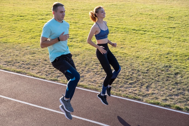 Junge Paare von fitten Sportlerjungen und -mädchen, die laufen, während Übung auf roten Spuren des öffentlichen Stadions im Freien tun.