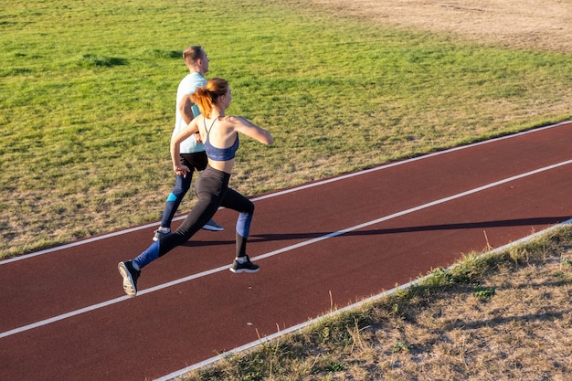 Junge Paare von fitten Sportlern Jungen und Mädchen laufen, während Übung auf roten Spuren des öffentlichen Stadions im Freien.