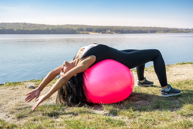 Junge passende Frau in Sportbekleidung während der Fitnesszeit und beim Trainieren mit Ball am See. Gesunder Lebensstil.