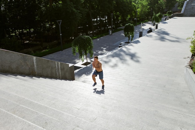 Junge passende männliche Läufer, die draußen die Treppe rütteln. Cardio-Training. Gesunder Lebensstil