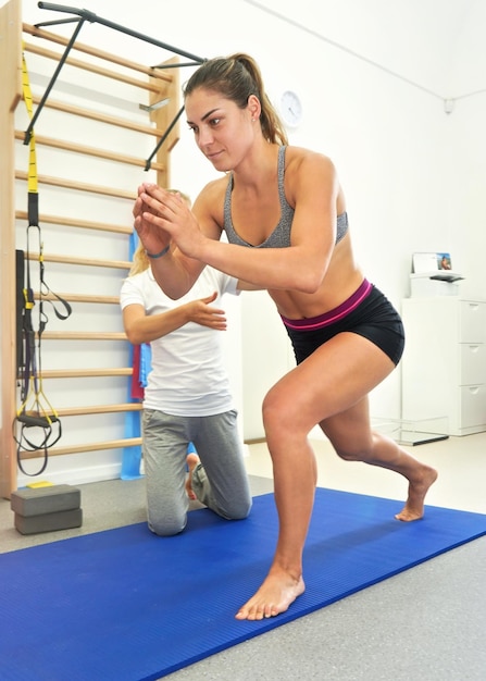 Junge Physiotherapeutin trainiert mit ihrer Patientin und überprüft sie, während sie sich auf einem Knie nach vorne beugt