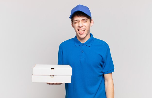 Junge Pizza liefert Jungen mit fröhlicher, sorgloser, rebellischer Haltung, Scherzen und herausstreckender Zunge, Spaß haben