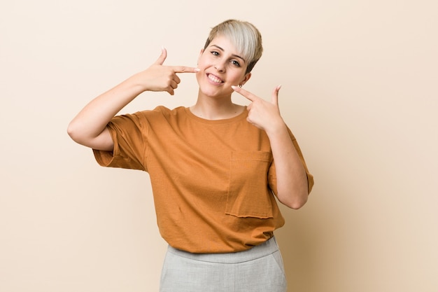 Junge plus Größenfrau mit dem kurzen Haar lächelt und zeigt Finger auf Mund.