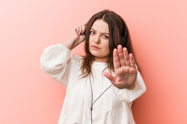 Junge plus hörende musik der kurvigen frau der größe mit den kopfhörern, die mit der ausgestreckten hand zeigt das stoppschild stehen und verhindern sie.