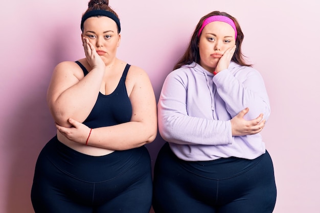 Junge Plus-Size-Zwillinge, die Sportkleidung tragen, denken müde und gelangweilt mit Depressionsproblemen mit verschränkten Armen.