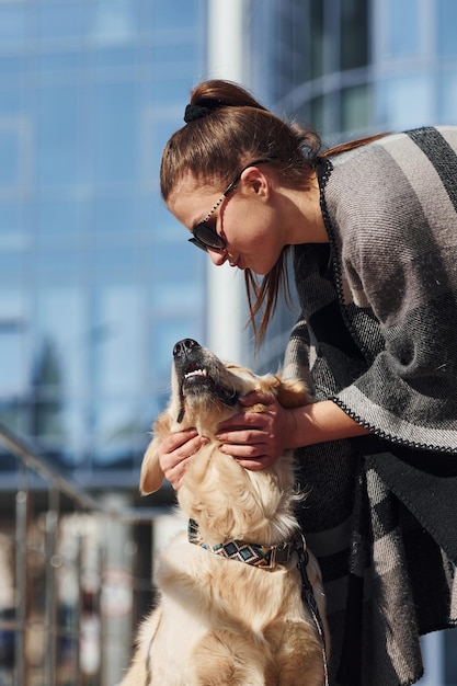 Junge positive Frau hat Spaß mit ihrem Hund, wenn sie draußen in der Nähe des Geschäftsgebäudes spazieren geht