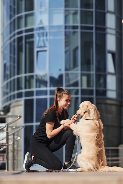 Junge positive Frau hat Spaß und macht Tricks mit ihrem Hund, wenn sie im Freien in der Nähe des Geschäftsgebäudes spazieren geht