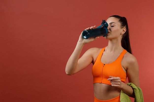 Junge positive Frau im orangefarbenen Fitness-Sport-Outfit-Tuch mit Flasche Wasser