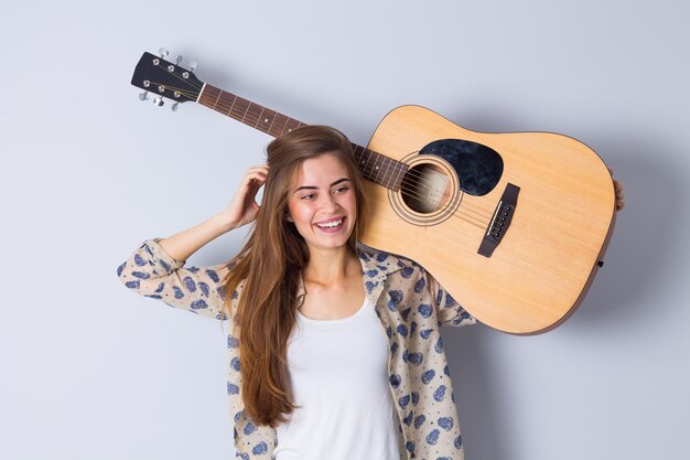 Junge positive Frau in beiger Bluse mit Gitarre auf grauem Hintergrund im Studio