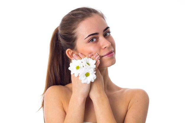 Junge positive Frau mit langem Pferdeschwanz, der weiße Blumen auf weißem Hintergrund im Studio hält