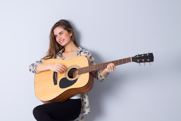 Junge positive Frau mit langen Haaren in brauner Jacke, die im Studio Gitarre spielt