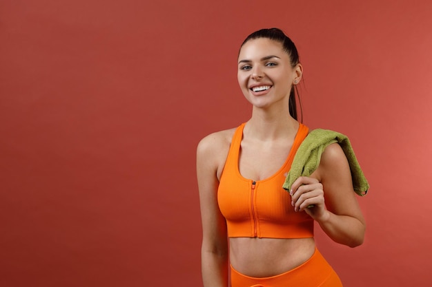 Junge positive lächelnde Frau im orangefarbenen Fitness-Sport-Outfit-Tuch Studio isoliert erschossen