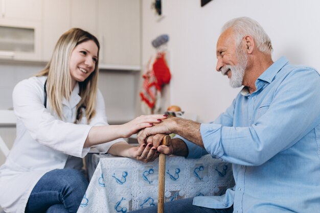 Junge positive Pflegekraft, die sich um den älteren Mann im Pflegeheim kümmert.