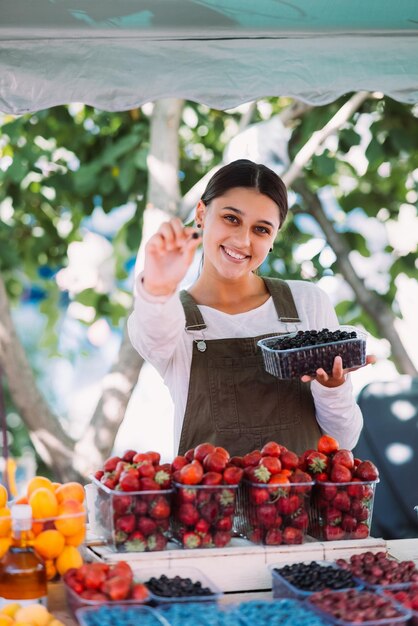 Junge positive Verkäuferin bei der Arbeit, die Johannisbeeren in ihren Händen hält