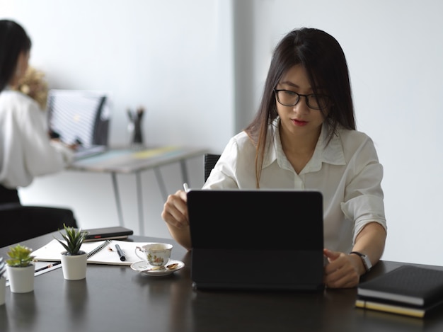 Junge professionelle Geschäftsfrau konzentrieren sich auf ihre Arbeit, während sie mit Tablette arbeiten