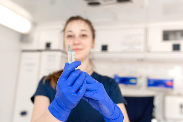 Junge professionelle Krankenschwester in der medizinischen Uniform, zeigen Spritze in ihren Händen am Krankenwagenhintergrund.