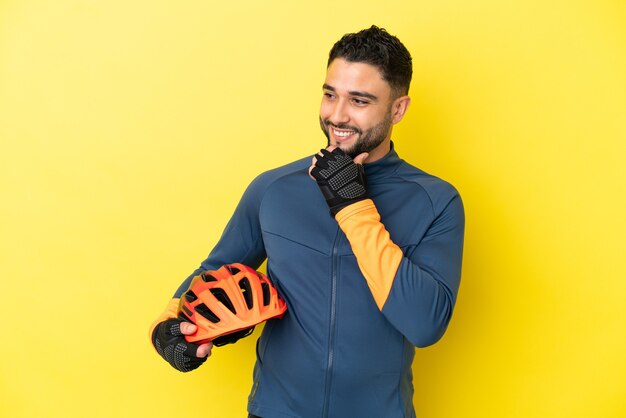 Junge Radfahrer arabischer Mann isoliert auf gelbem Hintergrund zur Seite schauen und lächeln