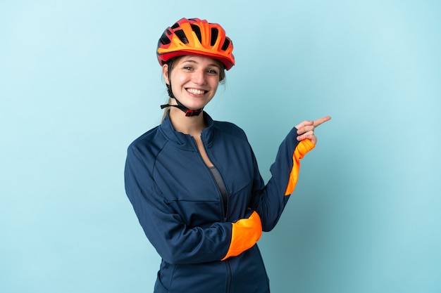 Junge Radfahrerfrau lokalisiert auf blauem Hintergrund, der Finger zur Seite zeigt